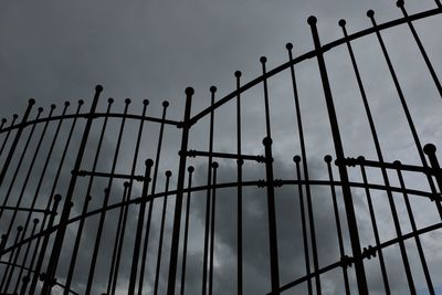 Low angle view of metallic fence against cloudy sky