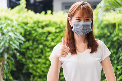 Portrait of young woman wearing mask gesturing outdoors
