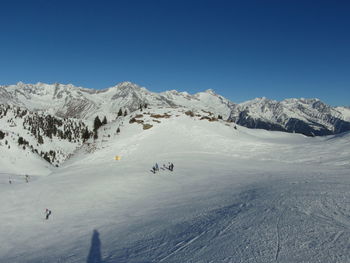 High angle view of people skiing on snowcapped mountains against clear blue sky