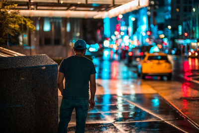 Rear view of man standing on city street during rainy season