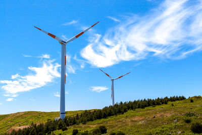 Low angle view of wind turbines on field against sky