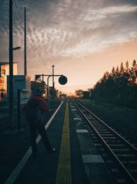 Man standing on railroad tracks against sky during sunset