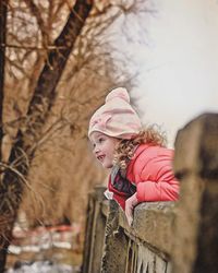 Cute smiling girl standing by railing against trees