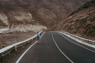 Rear view of woman walking on country road against mountain