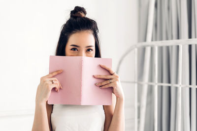 Portrait of woman holding book against wall