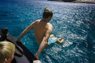 Boy looking at shirtless man jumping into sea from boat