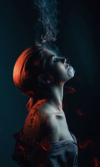 Side view of woman smoking against black background