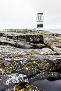 Lighthouse on rocky shore against sky