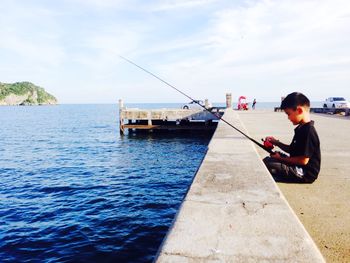 Side view of man fishing in sea against sky