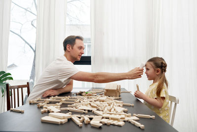 Father checking body temperature of daughter playing with wooden blocks