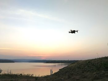 Airplane flying over landscape against sky during sunset