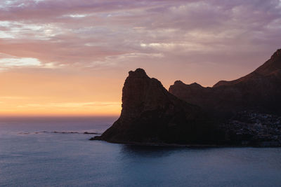 Rock formation in sea against sky during sunset