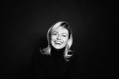 Portrait of smiling young woman against black background