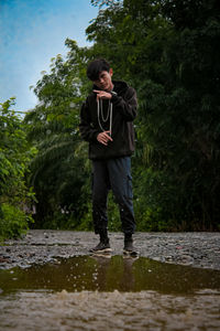 Full length of young man looking away while standing against trees