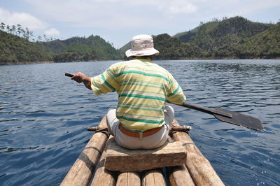 Rear view of man sitting on boat sailing in lake