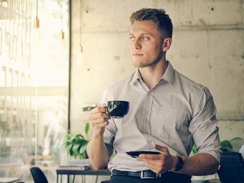 Young man looking away while holding coffee cup