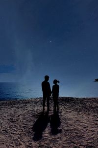 Rear view of men on beach against sky at night