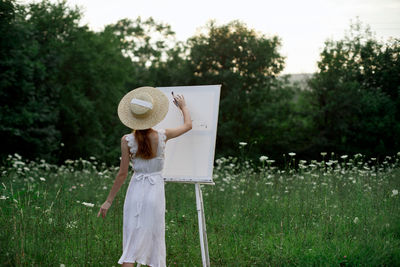 Woman wearing hat standing on field against trees