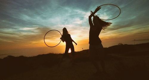 Women playing with plastic hoop on field against sky during sunset