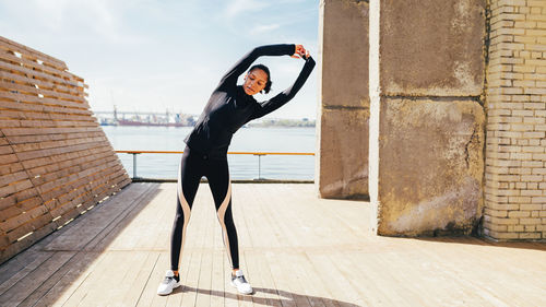 Young woman stretching on footpath against sky