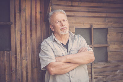 Thoughtful senior man standing against barn