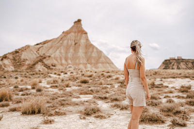 Rear view of woman standing on field against rock mountain