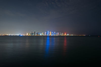 Illuminated city by sea against sky at night