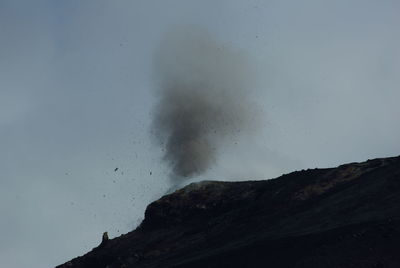 Low angle view of smoke emitting from silhouette mountain against sky