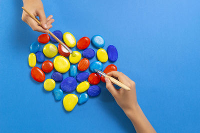 Low section of woman holding multi colored balloons against blue background