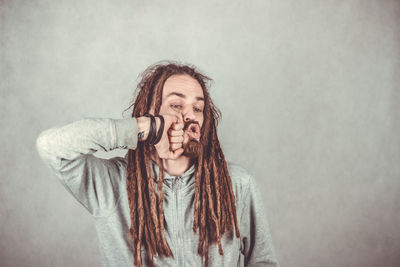 Young man with dreadlocks making face against wall