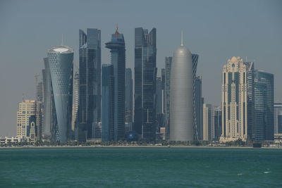 Sea by modern buildings against sky in city