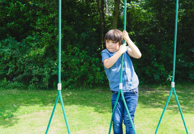 Cute boy looking away while standing on rope against plants