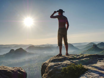 Cowboy style hiker man on cliff watching over misty morning valley to sun. man body with akimbo arms