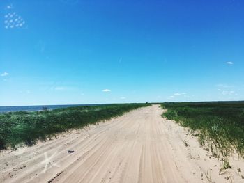 Road leading towards beach against blue sky