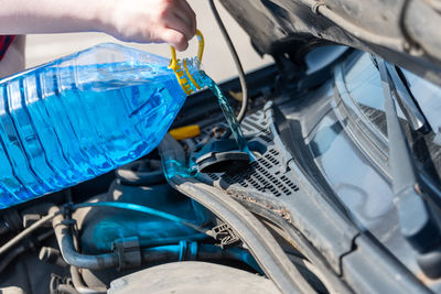 Woman hands pouring blue windshield washer fluid into a car's tank. close up.