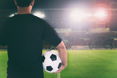 Rear view of referee holding soccer ball at stadium during night