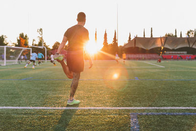 Rear view of man playing soccer on field during sunset