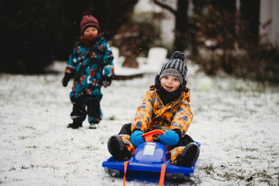 Young child sitting on sleigh smiling on snowy day in backyard