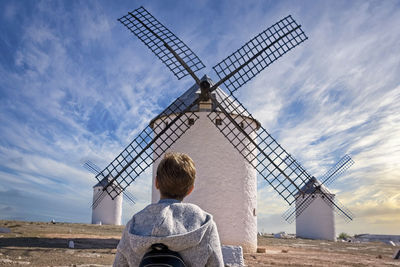 Rear view of mature woman looking at traditional windmills against cloudy sky