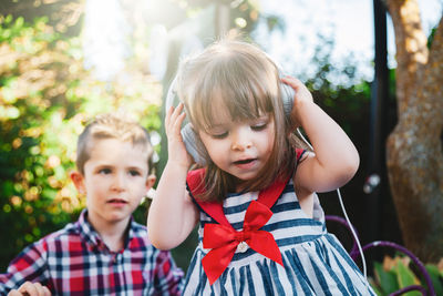 Close-up of cute sister listening music on headphones with brother standing in background