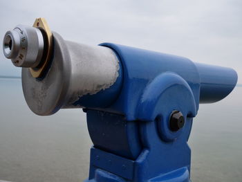 Close-up of coin-operated binoculars by sea against sky