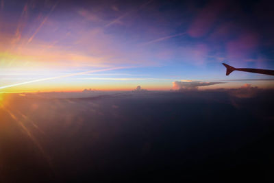 Airplane flying over landscape against sky during sunset