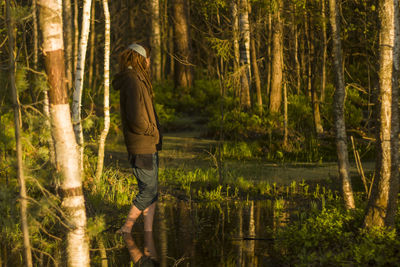 Side view of woman standing in lake against trees at forest