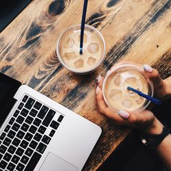 Cropped image of woman with cold coffee by laptop at table