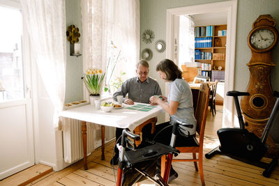 Mature female healthcare worker playing cards with retired senior man at table in nursing home