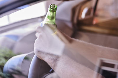 Close-up of man hand holding beer bottle sitting in car