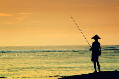 Silhouette man fishing in sea against sunset sky