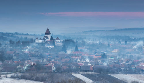 Fog covered town against sky during sunset