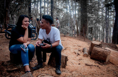 Full length of friends sitting on land in forest