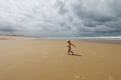 Full length of shirtless baby girl walking on sand at beach against sky